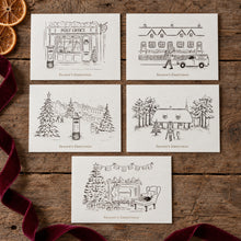 Load image into Gallery viewer, Five Christmas-themed greeting cards arranged on a rustic wooden surface with dried orange slices and a burgundy ribbon. The cards feature black line drawings of post office scenes, houses, trees, and a cozy living room, each labeled 'Season's Greetings'.