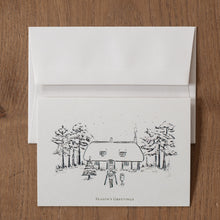 Load image into Gallery viewer, Christmas card with a black and white illustration of a house and trees on a wooden surface
