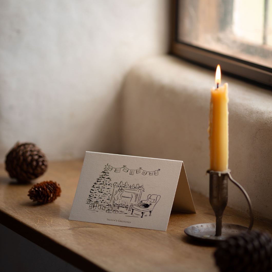 Greeting card with Christmas illustration on a wooden surface with a candle and pinecones.