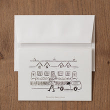 Load image into Gallery viewer, Christmas card with a postal van and building illustration on a wooden surface
