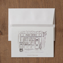 Load image into Gallery viewer, Greeting card with a post office illustration and &#39;Season&#39;s Greetings&#39; text, on a wooden surface.
